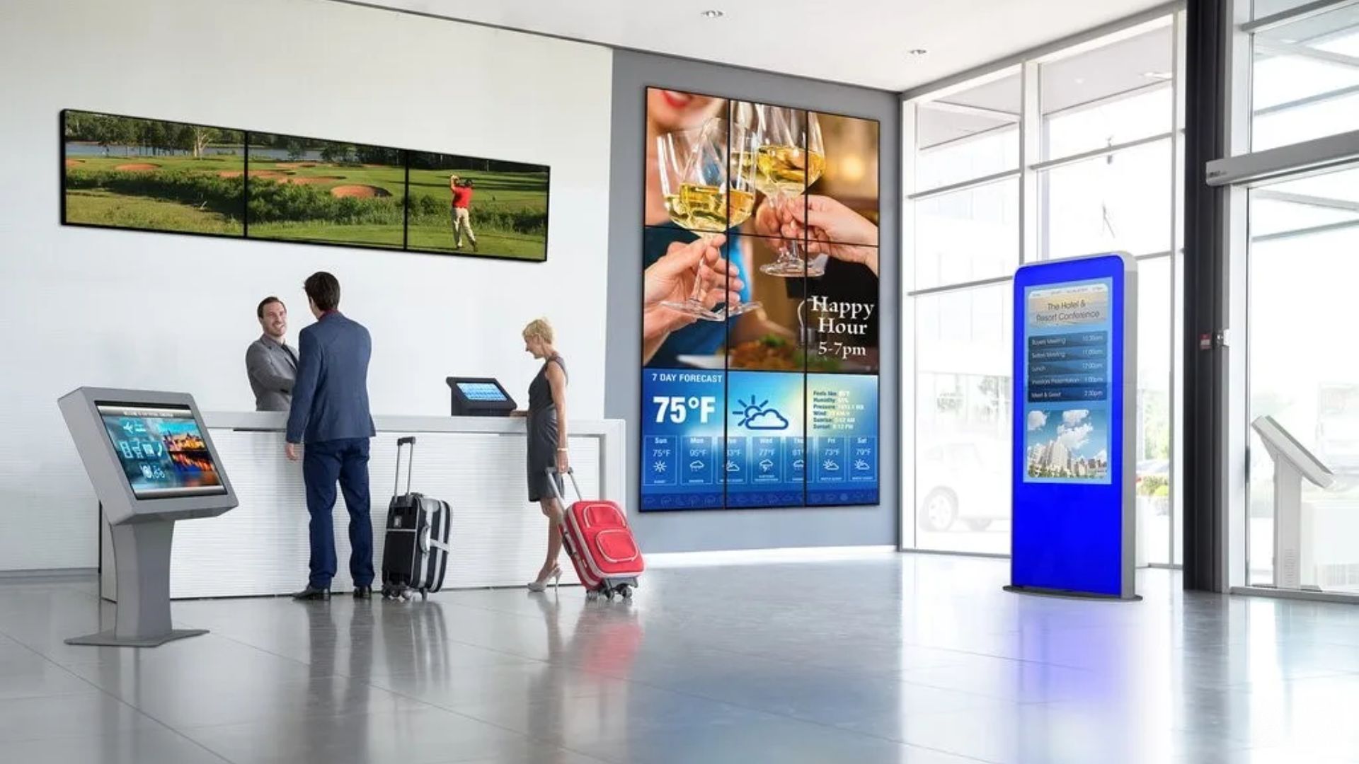 A hotel lobby with a video wall, a check-in kiosk, a tablet at the desk and a tall information totem, all showing managed content.
