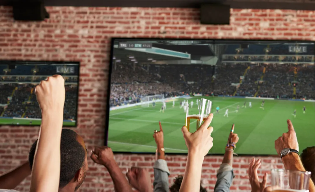 Fans cheering a football match on a bar screen.