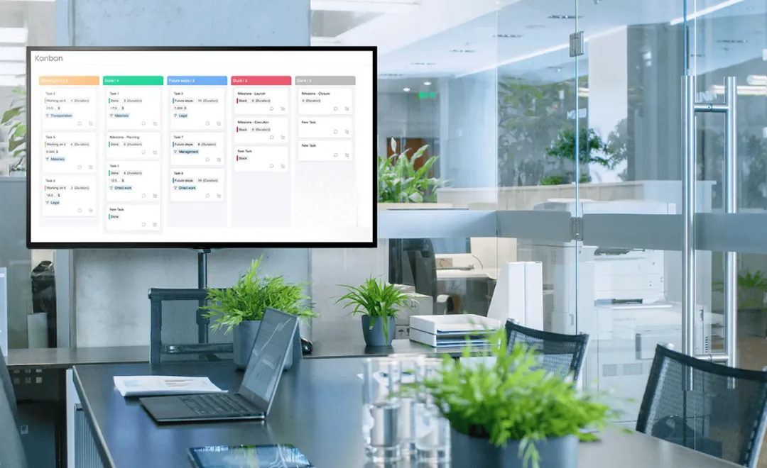 A project board on a screen in an open-plan office.