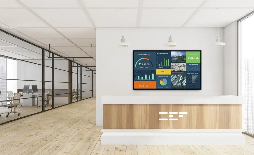 A dashboard on a screen above the reception desk of a bright office.