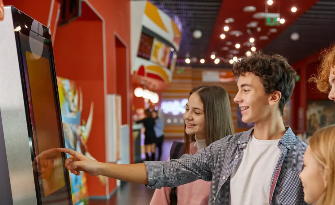 Teenagers using a touch-screen kiosk in a cinema lobby.